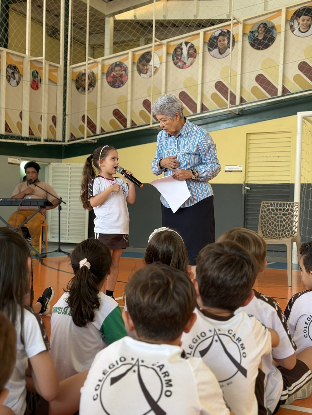 Aluna do Carmo ao microfone durante celebração no ginásio